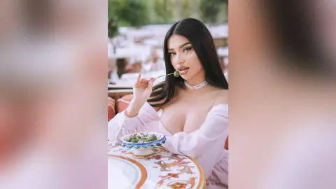 Young woman in a pink blouse eating an olive at an outdoor garden party setting.