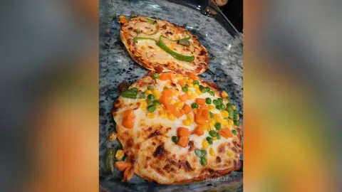 Homemade vegetable pizza topped with melted cheese, green peppers, and corn on a marble countertop.
