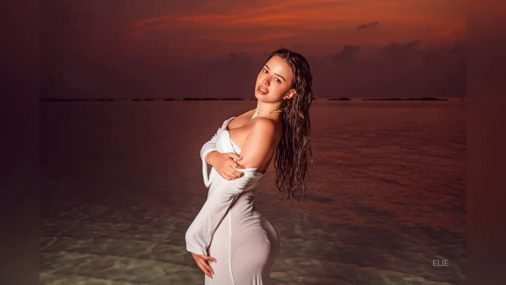 Young woman in an orange bikini standing in turquoise tropical ocean water near luxury overwater bungalows.