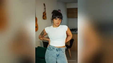 Confident young woman in a white crop top and light blue jeans posing in a cozy living room.