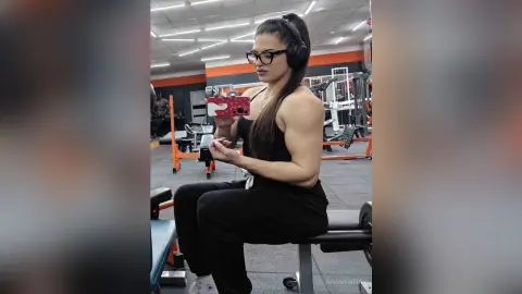 Athletic woman in black gym wear taking a mirror selfie in a modern fitness center.