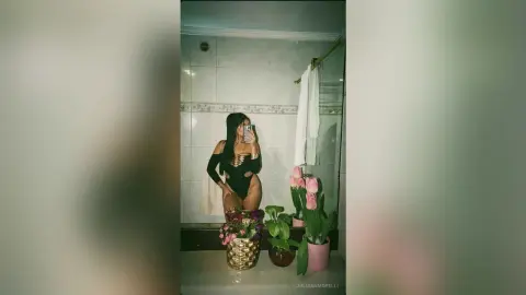Woman in a black cutout bodysuit taking a mirror selfie in a modern bathroom with pink tulips.