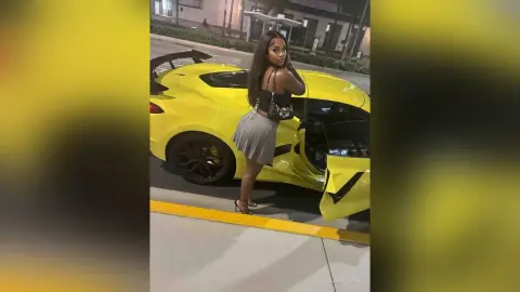Stylish woman in a black tank top and pleated skirt posing by a bright yellow luxury sports car at night.
