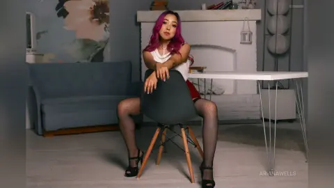Young woman with pink hair in a white top and black tights sitting on a chair in a bright modern living room.