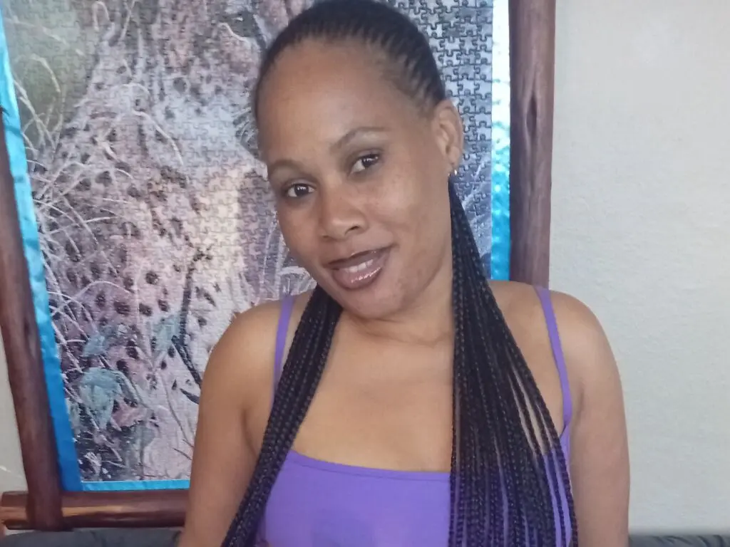 CathySimons smiles while wearing a purple tank top with her long black braids hanging down her shoulders.