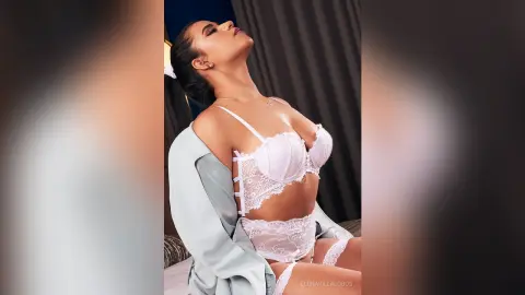 Elegant woman in white lace lingerie and a light blue robe posing in a moody indoor setting.