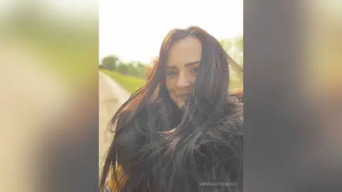 Smiling woman with long dark hair outdoors in soft natural sunlight.