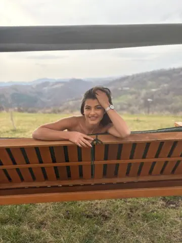 Smiling young woman relaxing on a wooden bench in a scenic mountain meadow during a peaceful sunset.