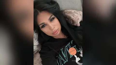 Young woman with long dark hair wearing a black graphic t-shirt relaxing on a couch in a cozy indoor setting.