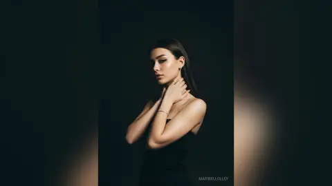 Elegant woman in a black dress posing against a dark background with moody, dramatic studio lighting.