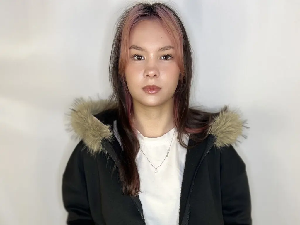 Glamorous woman with high ponytail and glowing makeup posing in a warm, indoor setting.