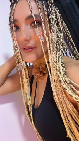 Woman with long blonde box braids wearing a black halter top and floral choker in a bright setting.