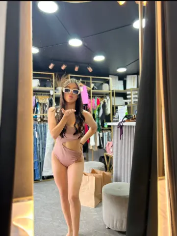 Stylish woman in a mauve bodysuit posing in a modern clothing boutique with bright lighting.