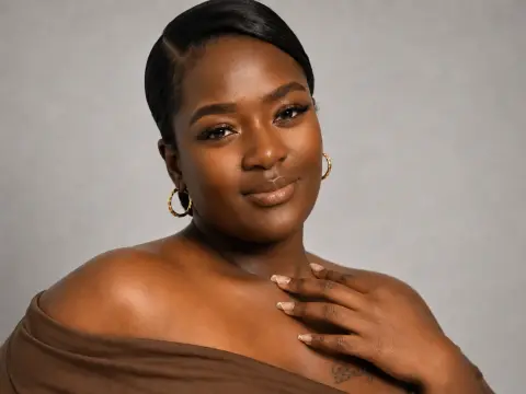 Smiling Black woman with gold hoop earrings and sleek hair posing in a brown off-the-shoulder top.