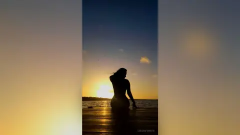 Silhouette of a woman sitting on a wooden pier at sunset overlooking a calm ocean under a golden sky.