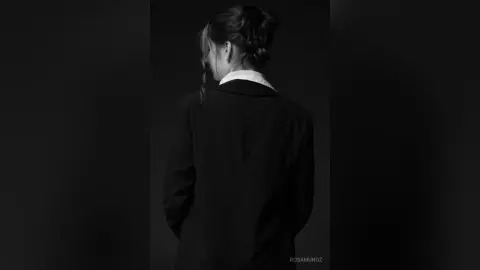 Moody black and white portrait of a woman in a dark blazer looking away in a minimalist setting.