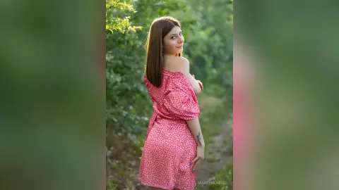 MarryMenedez looks over her shoulder in a pink floral dress while posing outdoors in a garden.