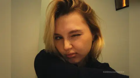 Blonde woman in a dark navy sweater winking playfully in a cozy indoor setting.