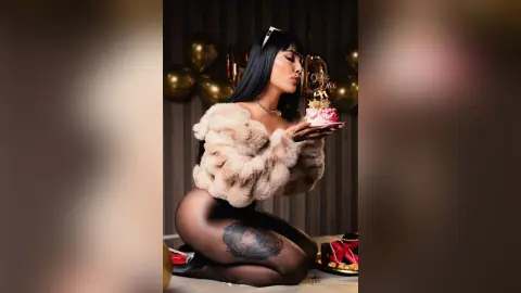 Glamorous woman in a beige faux fur jacket and black tights celebrating with a pink cake in a festive setting.