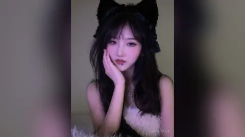 Young woman with cat ears and dark hair wearing a white lace outfit in a soft, dreamy indoor setting.