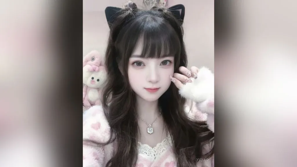 YiQiao — YiQiao wears a pink fuzzy sweater and a black bow headband while posing in her room.