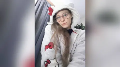 Young woman with glasses wearing a cozy white Hello Kitty hooded fleece jacket in a relaxed indoor setting.
