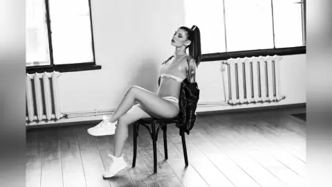 Stylish woman in Calvin Klein underwear and sneakers sitting on a chair in a bright, minimalist studio.