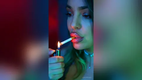 DorothyLake — DorothyLake holds a lit lighter to a cigarette in her mouth under blue and red lighting.