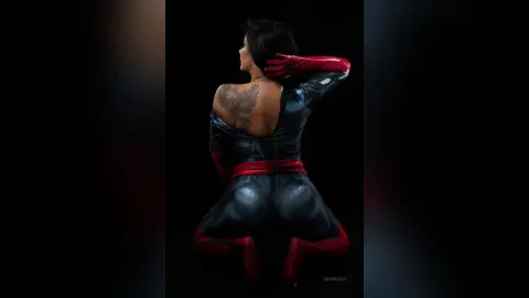 MissyJolie poses from behind wearing a tight black and red bodysuit that shows off her back and tattoo.