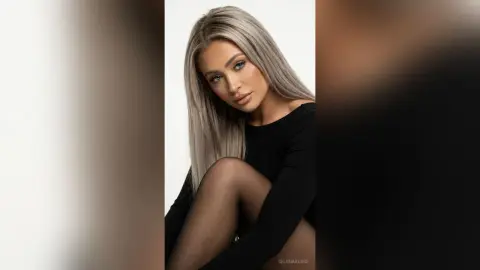 Elegant woman with long silver hair wearing a black long-sleeve top in a minimalist studio setting.