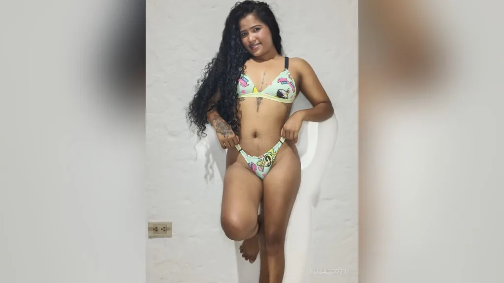 Smiling woman with long wavy hair wearing a lime green bikini set in a minimalist indoor setting.