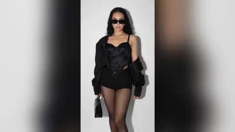 Stylish woman in a black corset top, shorts, and sunglasses posing against a white background.