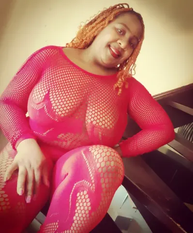 Smiling woman in a bright pink fishnet bodysuit posing indoors with a joyful mood.