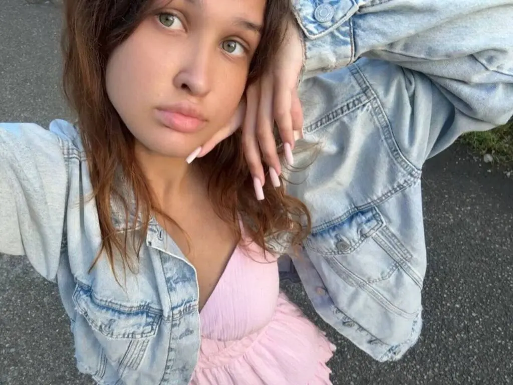 JazminHalajian wearing a light pink top and a light blue denim jacket, posing with her hand against her face outdoors.