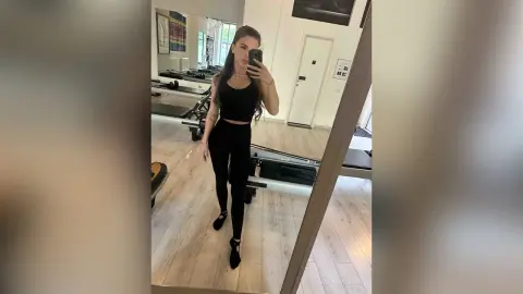 Young woman in black athletic wear taking a mirror selfie in a bright modern home gym.