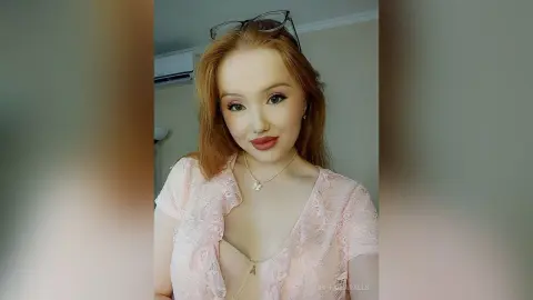 Redheaded woman in a pink lace outfit posing with a soft, romantic look in a bright indoor setting.