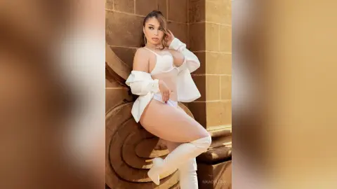Glamorous woman in white lingerie and tall boots posing against a classic stone architectural background.