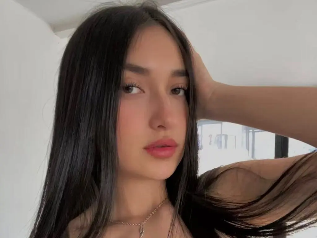 Young woman with long dark hair and natural makeup posing in a bright indoor setting.