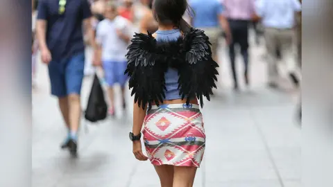 Woman wearing black angel wings and a patterned skirt walking through a crowded city street.