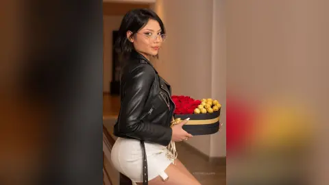 RebecaVillalobos wears a black leather jacket and white shorts while holding a box of red and gold roses.