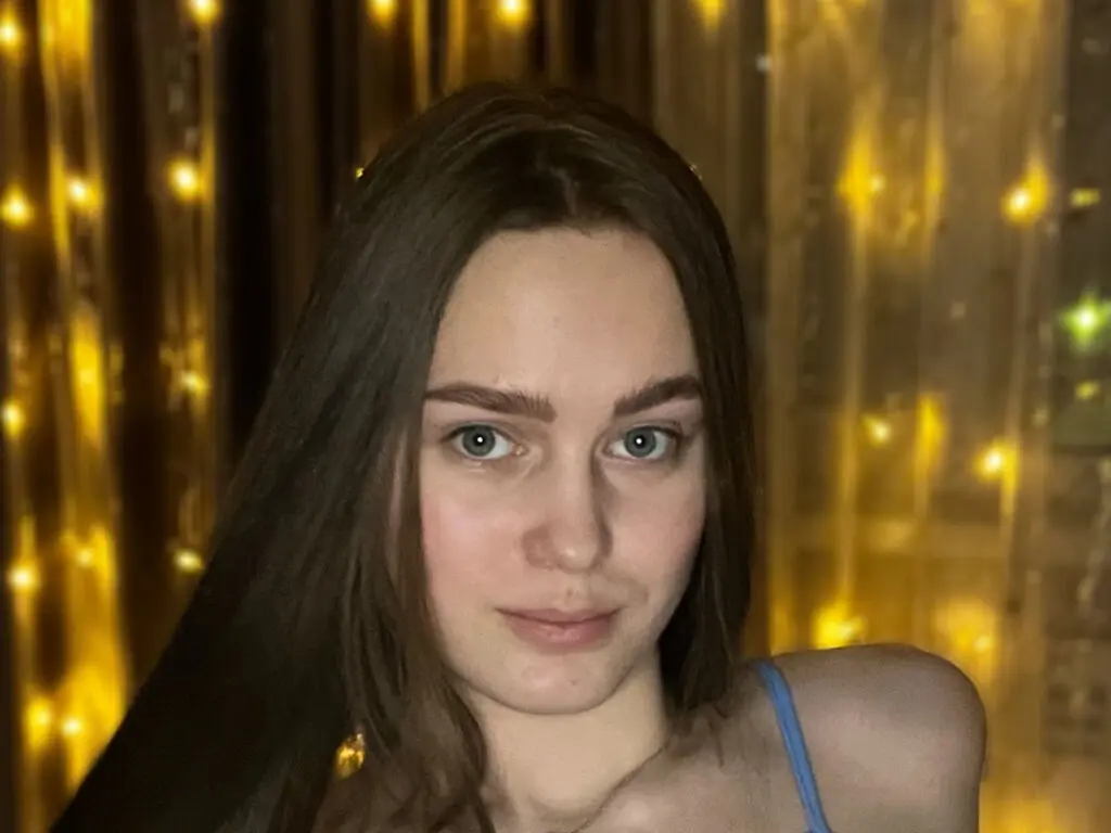 Young woman with long brown hair in a blue top posing against a warm, glowing bokeh light background.