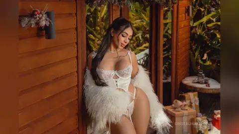 Glamorous woman in white lace lingerie and a fluffy faux fur coat posing in a lush tropical garden setting.