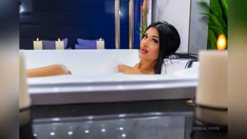 Relaxed woman enjoying a luxury bubble bath in a modern bathroom with glowing candles.