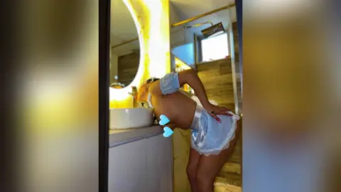 Young woman in a white summer outfit leaning over a bathroom sink in a bright, modern interior.