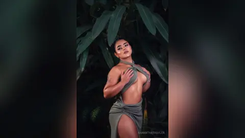 Elegant woman in a sage green halter dress posing amidst lush tropical greenery in a moody outdoor setting.