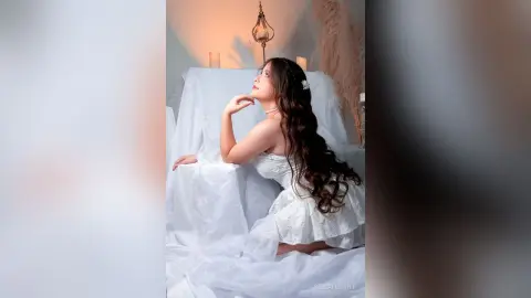 Elegant woman in a white lace dress sitting in a dreamy, ethereal setting with soft candlelight.