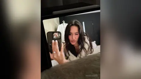 Young woman in a cozy white sweater taking a moody mirror selfie in a modern bedroom.
