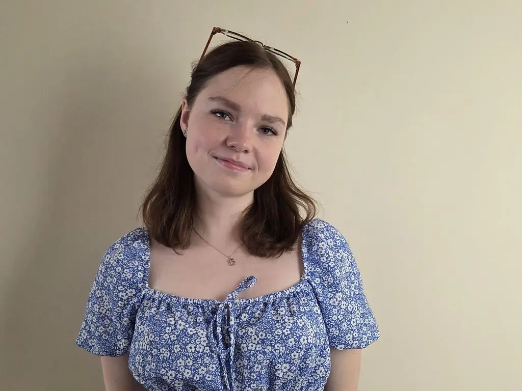 Smiling young woman in a blue floral puff-sleeve blouse posing against a neutral beige wall.