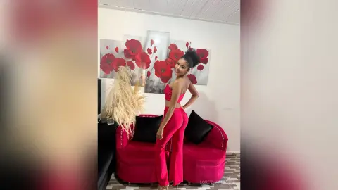 LoreyHamilton — Smiling woman in a stylish red jumpsuit sitting on a pink velvet sofa in a modern living room.
