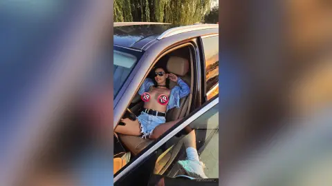Stylish woman in denim shorts and a light blue shirt sitting in a car during golden hour.